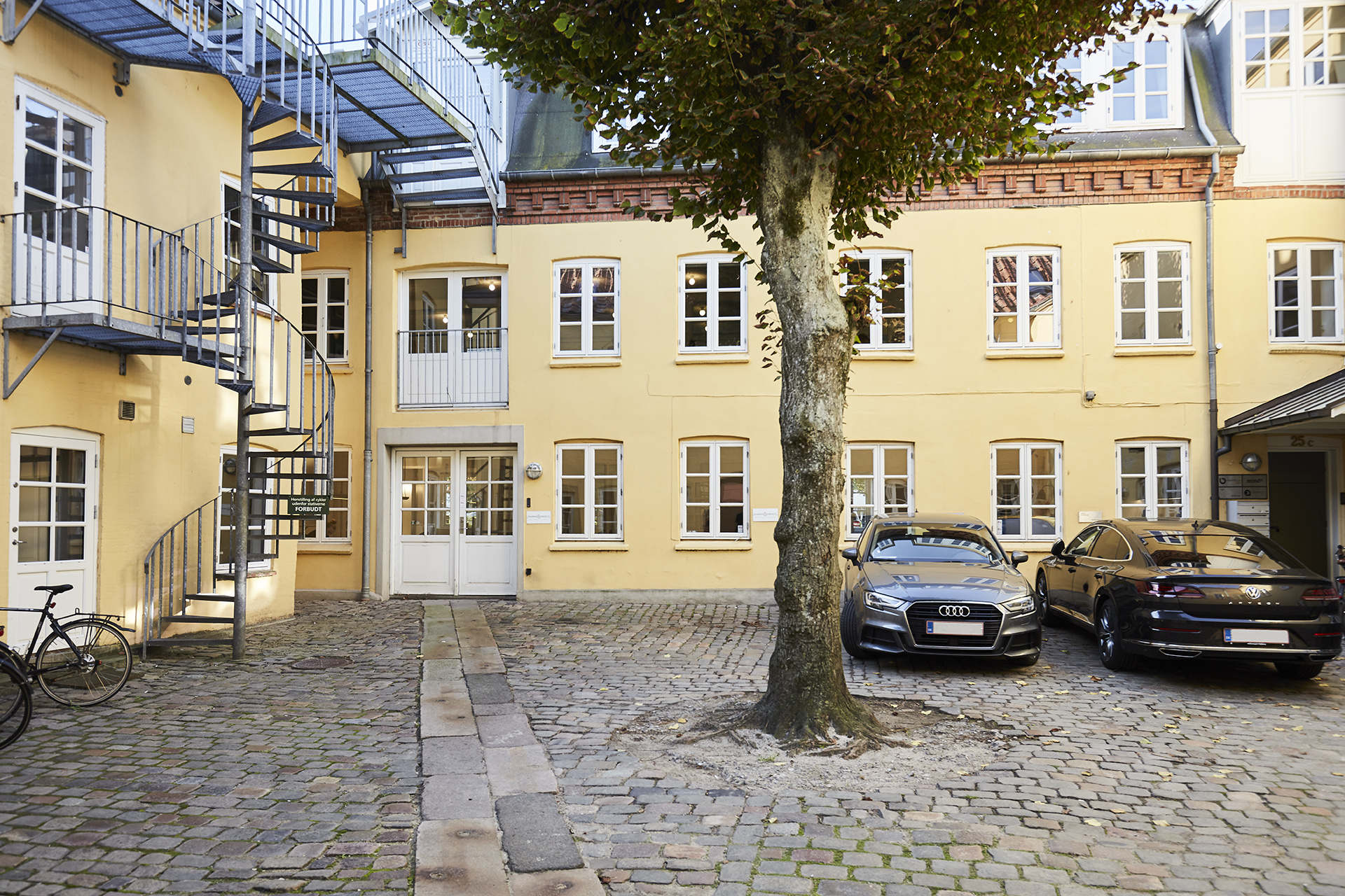 Det hyggelige brostensbelagte gårdmiljø med det flotte lindetræ i midten, hvor bødkerens spor stadig ligger til venstre.